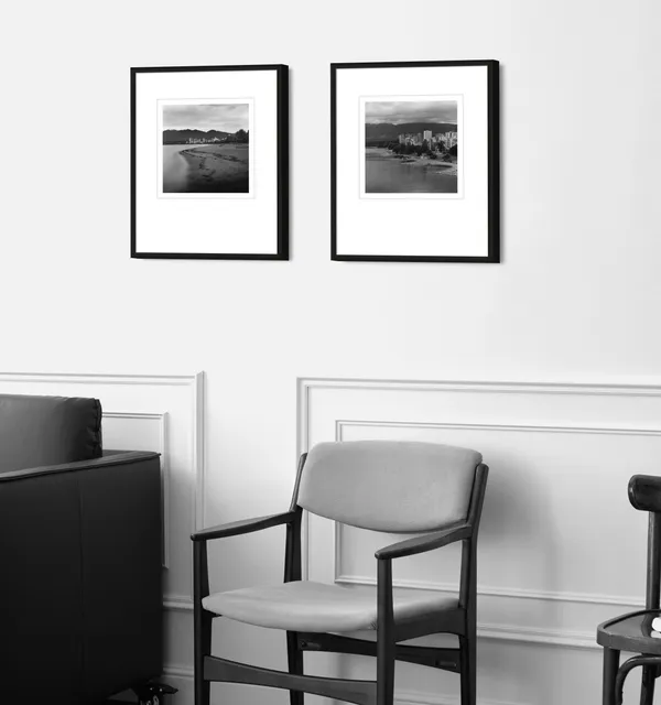 A pair of framed silver gelatin prints of Vancouver shorelines hung above a mid-century armchair.