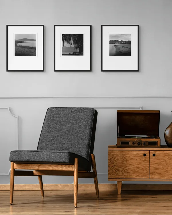 Three framed 10 × 10 in. silver gelatin prints of Vancouver beaches, hung as a triptych above a mid-century sideboard in a living room. Shop available prints.